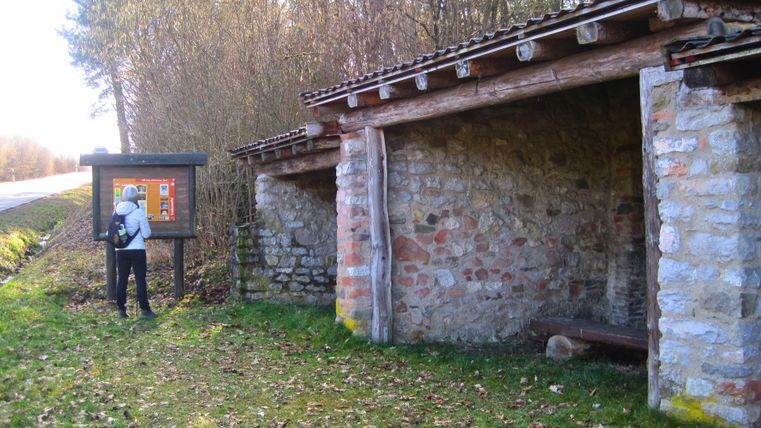 Person liest Infotafel neben historischem Kalkofen in Nohn.