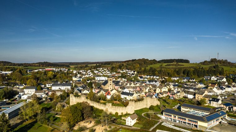 Luftaufnahme von Hillesheim mit historischer Stadtmauer und Kirche, umgeben von grüner Landschaft.