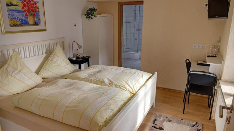 Ein gemütliches Schlafzimmer mit einem großen Bett und gelben Bettwäsche. Es gibt einen Schreibtisch, einen Stuhl und ein Badezimmer in der Nähe.