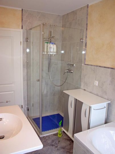 Een moderne badkamer met een glazen douche en een wastafel. Op de achtergrond is een bad te zien.