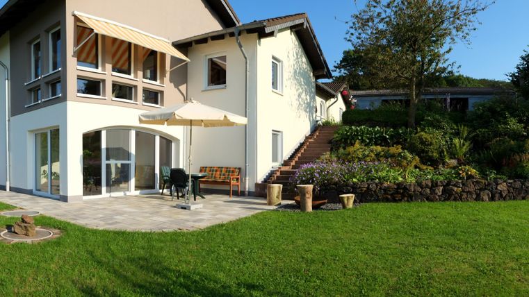 Ein schönes Haus mit einem gepflegten Garten. Es gibt eine Terrasse mit einem Sonnenschirm und blühenden Pflanzen.