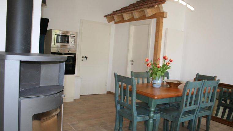 Een gezellige eethoek met een houten tafel en groene stoelen bevindt zich in een lichte ruimte. Een oven en een bloemvaas completeren de inrichting.