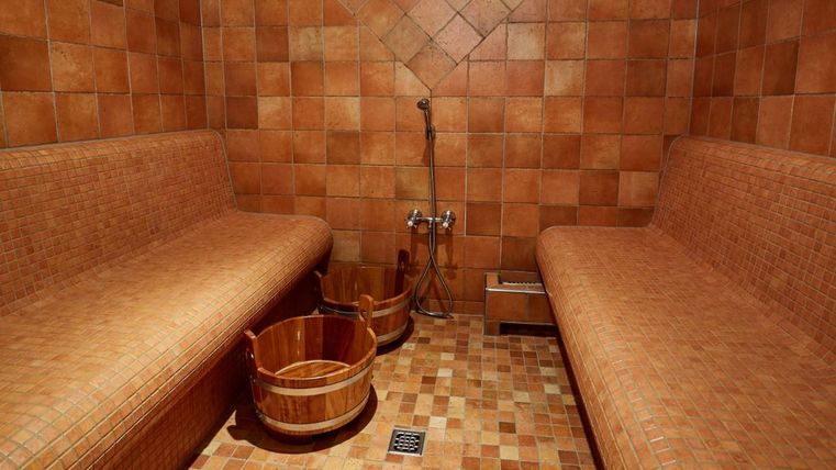 Ein entspannender Raum mit zwei Bänken aus gefliesten Materialien. In der Ecke stehen Holzbottiche für Wasser.