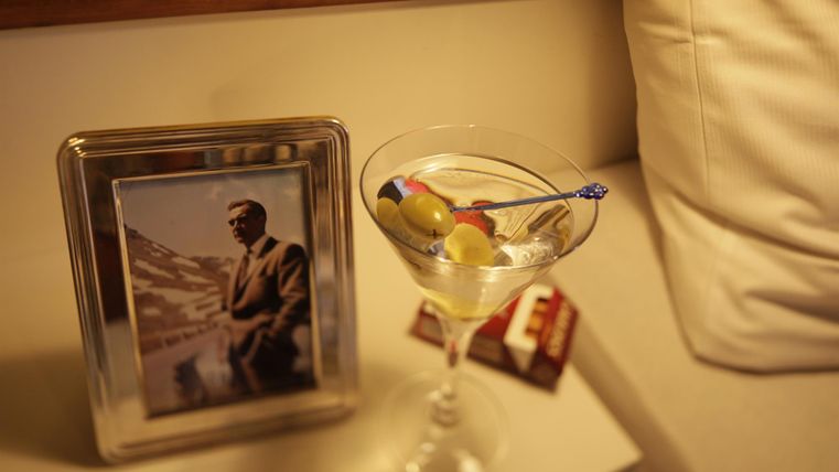 Un élégant cocktail avec des olives est posé sur une table à côté d'une photo encadrée. En arrière-plan se trouve un canapé clair.