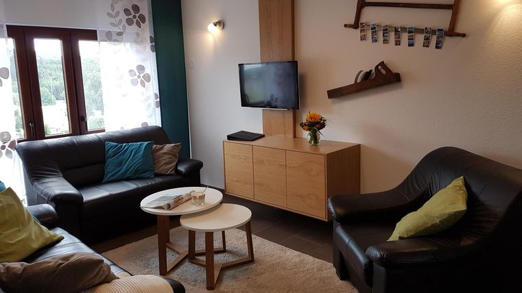 Ein modernes Wohnzimmer mit zwei schwarzen Sofas und einem kleinen Tisch. An der Wand ist ein Fernseher und eine dekorative Ablage installiert.