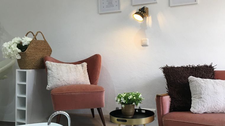 Une pièce confortable avec deux fauteuils roses et une table basse en bois. Sur la table se trouve un bol avec des fleurs et une petite plante.