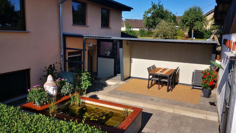 Ein schöner Garten mit einem Teich und einer Terrasse. Es gibt einen Tisch mit Stühlen und üppige Pflanzen.