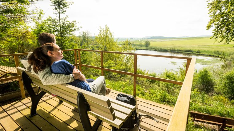 Paar sitzt auf einer Bank mit Blick auf das Eichholzmaar.