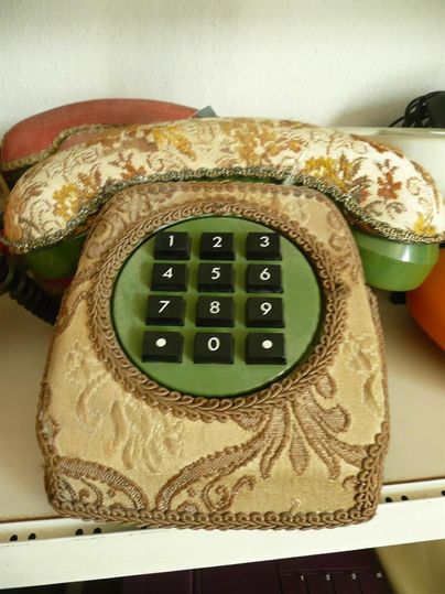 Ein antikes Telefon mit dekorativem Stoffbezug und Wähltasten auf einem Regal.
