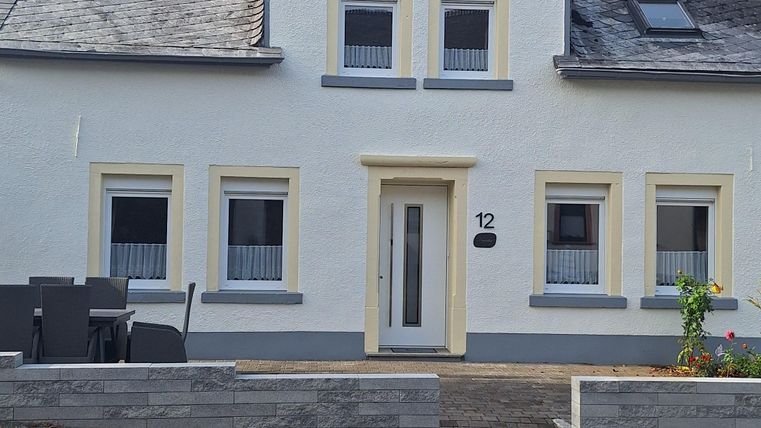 Ein einladendes, zweigeschossiges Haus mit hellen Wänden und einem Satteldach. Die Fenster sind symmetrisch angeordnet und es gibt einen kleinen Gartenbereich vor dem Haus.