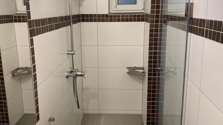 Ein modernes Badezimmer mit einer Dusche und weißen Fliesen. Die Einrichtung ist schlicht und elegant.