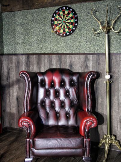 Un fauteuil en cuir élégant se trouve devant un mur en bois lambrissé. Au-dessus du fauteuil, il y a une cible de fléchettes.