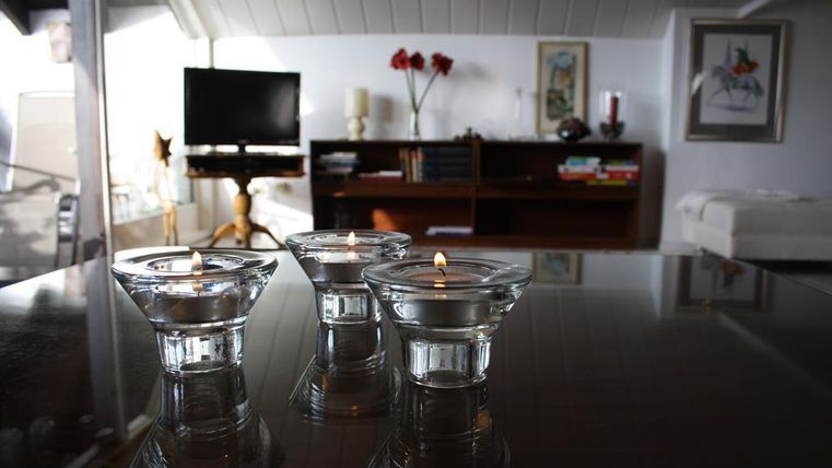 Drei Glas-Teelichter stehen auf einem Tisch in einem modernen Raum. Im Hintergrund sind Möbel und ein Fernseher sichtbar.