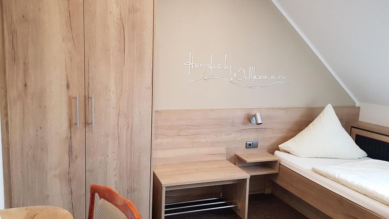 Ein einfaches Zimmer mit modernen Holzmöbeln. Es gibt ein Bett, einen Tisch und einen Schrank.