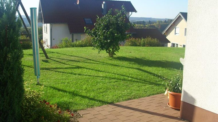 Ein schöner Garten mit grünem Rasen und einem Blick auf die umliegenden Häuser. Die Sonne scheint und der Himmel ist blau.