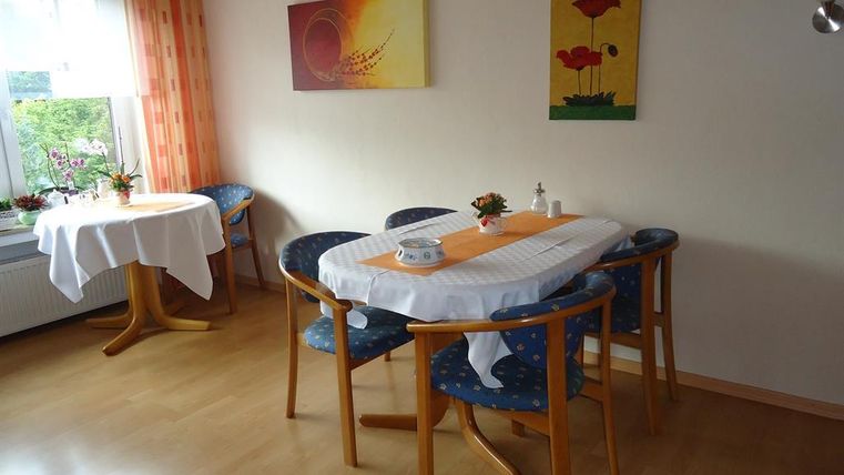 An inviting breakfast room with a table and chairs. Colorful pictures hang on the walls, and the windows let in a lot of light.