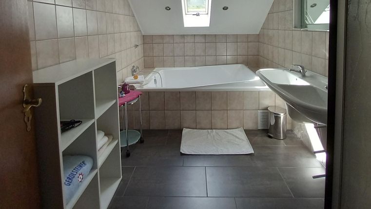 Ein modernes Badezimmer mit einer Badewanne und einem Waschbecken. Der Raum hat große Fenster und eine helle, freundliche Atmosphäre.