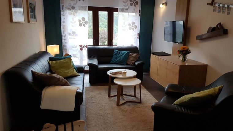 Ein gemütliches Wohnzimmer mit modernen Möbeln und einer ruhigen Atmosphäre. Die Fenster lassen viel Tageslicht herein, und die Dekoration schafft eine einladende Umgebung.