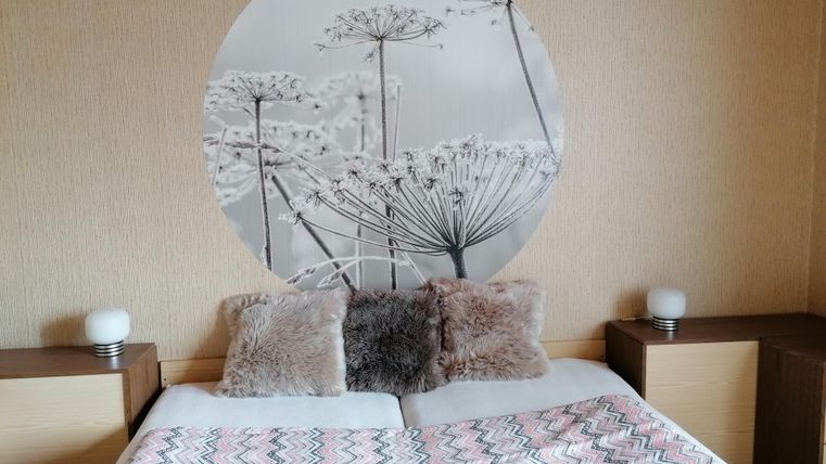 A cozy bedroom with a round wall mural of plants. The duvet is colorful and the pillows are in soft tones.