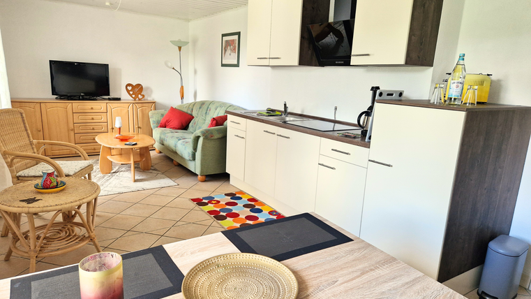 Un salon moderne avec une cuisine ouverte. La pièce est lumineuse et accueillante, avec un canapé, une table et plusieurs éléments décoratifs.