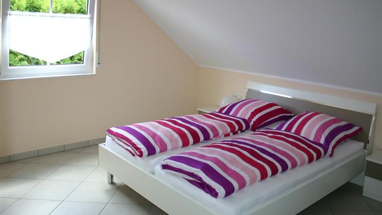 Een slaapkamer met een tweepersoonsbed en kleurrijke gestreepte dekens. De kamer heeft een raam dat natuurlijk licht binnenlaat en een lichte wandkleur.