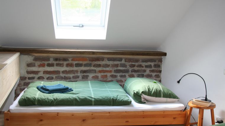 Een gezellige slaapkamer met een eenpersoonsbed en een licht dakraam. De beddengoed is groen en er staat een kleine houten stoel naast het bed.