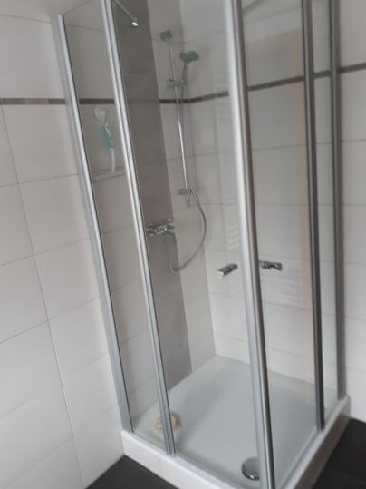 Eine moderne Duschkabine mit transparenten Glastüren. Die Wände sind gefliest und die Dusche hat eine moderne Armatur.