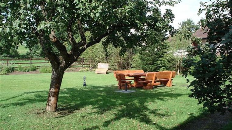 Un beau jardin avec un grand arbre et une table en bois avec des bancs. La pelouse est verte et bien entretenue.