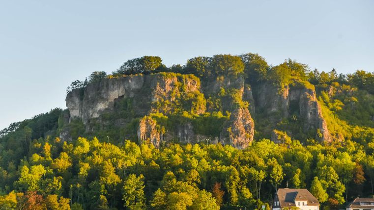 Felsformation Munterley im Abendlicht, umgeben von grünen Bäumen. Unten sind einige Häuser zu sehen.