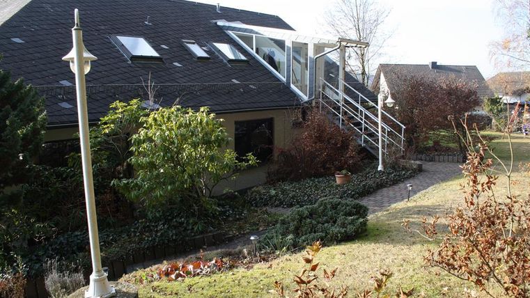 Ein modernes Haus mit einem gepflegten Garten. Im Hintergrund befinden sich Bäume und eine Treppe, die zur Terrasse führt.