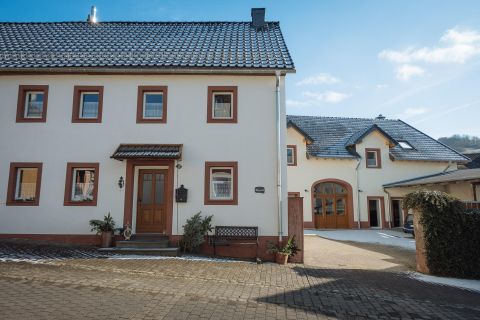 Ein modernes Wohnhaus mit einem roten Erker und einem angrenzenden Garagenbereich. Die Fassade ist hell und freundlich, umgeben von einem gepflasterten Hof.