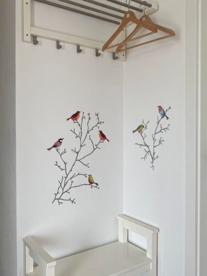 Un couloir lumineux avec un porte-manteau en bois. Sur le mur, de magnifiques motifs d'oiseaux sur des branches sont visibles.