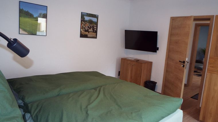 Ein gemütliches Schlafzimmer mit einem großen Bett und grüner Bettwäsche. An der Wand hängen Bilder, und ein Fernseher ist ebenfalls vorhanden.