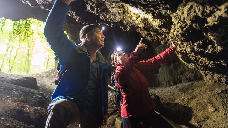 Zwei Personen mit Stirnlampen erkunden die Steinwände einer Höhle.