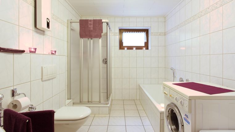 Ein modernes Badezimmer mit weißen Fliesen und einer Dusche. Im Raum befindet sich auch eine Badewanne und eine Waschmaschine.