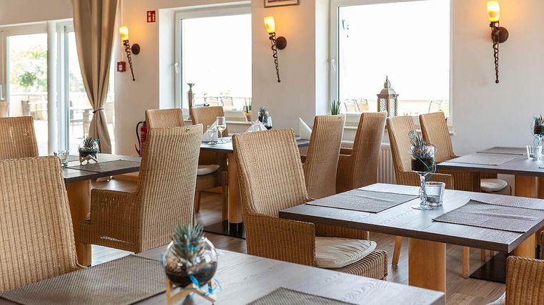 A modern restaurant with bright walls and wooden tables. The upholstered chairs and small plants on the tables create an inviting atmosphere.