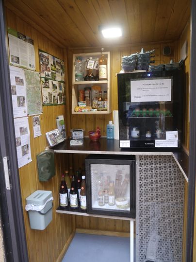 Innenraum einer kleinen Verkaufsbude aus Holz mit regionalen Lebensmitteln zur Selbstbedienung.