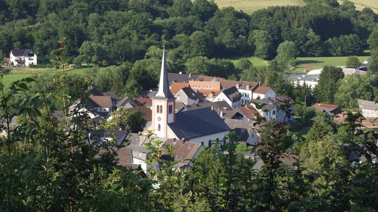 Blick auf Stadtkyll mit Kirche und umliegender Landschaft.
