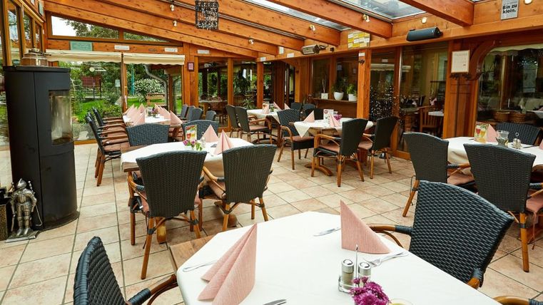 Ein einladender Restaurantbereich mit Holzwänden und einem Glasdach. Die Tische sind elegant mit weißen Tüchern und Servietten gedeckt.