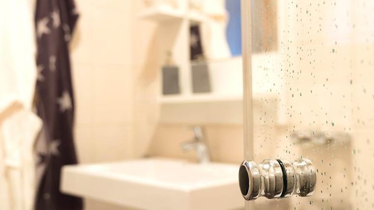 Ein modernes Badezimmer mit einem klaren Duschabtrennung und einem Waschbecken. Im Hintergrund sind Handtücher und eine große Spiegelfläche sichtbar.