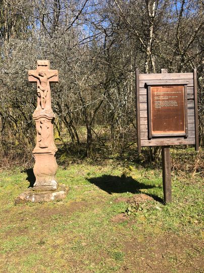 Steinkreuz und Infotafel im Wald.