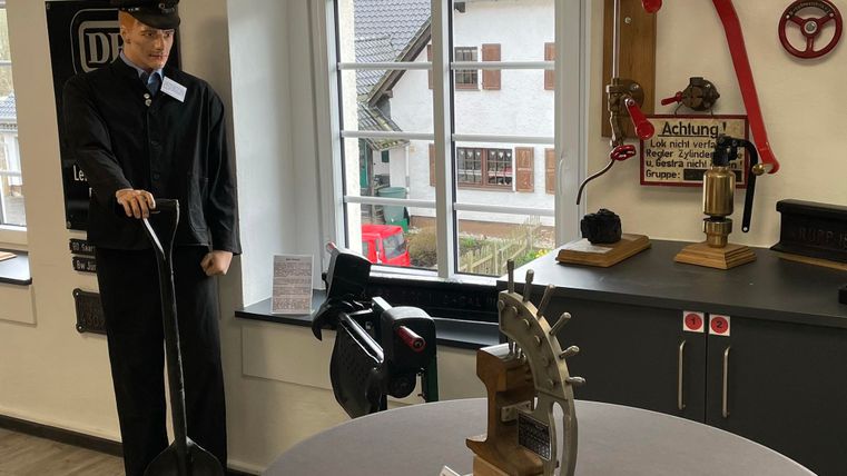 Museumsraum mit Schaufensterpuppe in Uniform, historischen Eisenbahnwerkzeugen an der Wand und einem Modell auf einem Tisch.