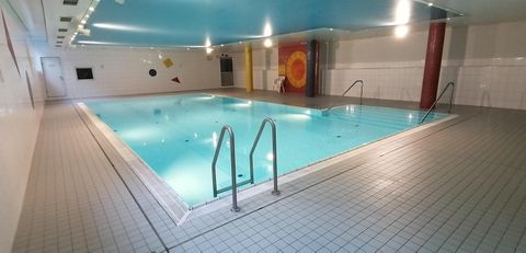 Ein Lehrschwimmbecken mit blauer Decke, bunten Wanddekorationen und zwei Einstiegsleitern. Die Wände sind weiß gefliest.