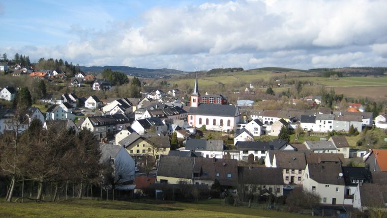 Panorama auf Stadtkyll mit Kirche und Hügeln im Hintergrund.