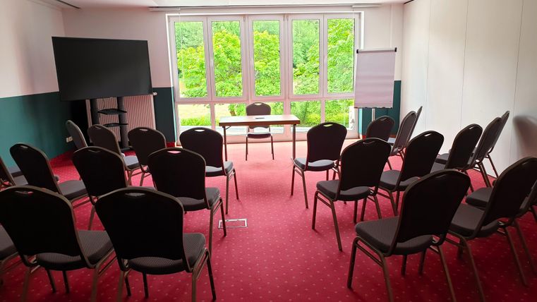 A conference room with chairs in rows and a table in the middle. Large windows offer a view of the green surroundings.