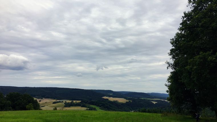 Un vaste paysage avec des collines douces et un ciel nuageux. Au premier plan, on peut voir de l'herbe verte et juteuse.