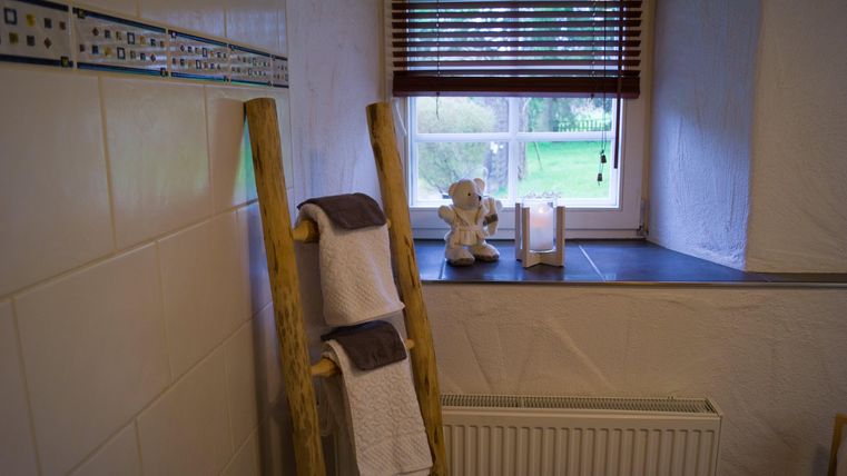 Een modern badkamer met een houten plank waarop frisse handdoeken liggen. Bij het raam staat een decoratieve figuur en een kaars die voor gezelligheid zorgt.