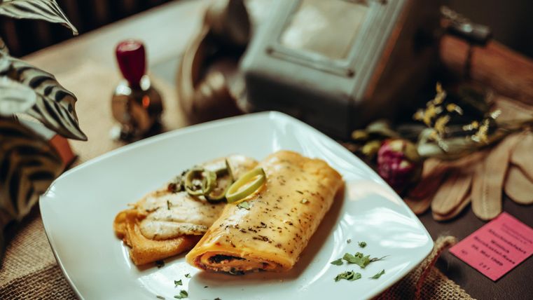 Ein Teller mit zwei herzhaften Omelettes, garniert mit Frühlingszwiebeln und Limettenscheiben. Im Hintergrund sind Küchenutensilien und Pflanzen zu sehen.