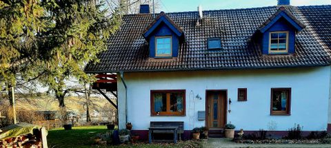 Ein gemütliches, zweigeschossiges Haus mit einem Satteldach und blauen Fensterrahmen. Der Eingang ist von einem kleinen Garten umgeben.