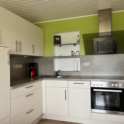 Une cuisine moderne avec des armoires blanches et un mur vert. Elle est équipée d'une cuisinière, d'un réfrigérateur et d'une hotte en acier inoxydable.